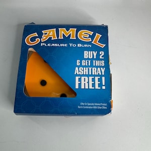 Może przedstawiać: Niebieskie pudełko z logo Camel i napisem „PLEASURE TO BURN”. W środku znajduje się pomarańczowa popielniczka w kształcie klina sera. Widoczny jest również napis „KUP 2 I OTRZYMAJ TĘ POPIELNICZKĘ GRATIS!”.
