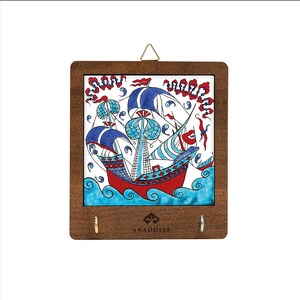 May include: A decorative wall hanging with a hand-painted nautical scene. It features a red ship, blue sails, and turquoise waves. The artwork is set within a dark brown wooden frame with two hooks and a gold-coloured hanger.