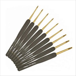 Peut inclure: Ensemble de crochets avec des manches noirs et des pointes dorées. Les manches portent la marque "Tulip" et des indications de taille, comme "4/0 2.50mm". Les crochets sont disposés en éventail sur fond blanc.