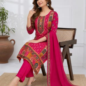 May include: A vibrant fuchsia three-piece ensemble featuring a long-sleeved tunic with a round neckline, intricate multi-colored geometric and floral patterns, matching solid fuchsia trousers, and a coordinating fuchsia dupatta with a decorative border.