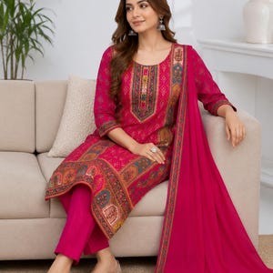 May include: A fuchsia three-piece outfit consisting of a long-sleeved tunic with a multi-colored geometric and floral print, solid fuchsia trousers, and a matching fuchsia dupatta with a decorative border along the edges.