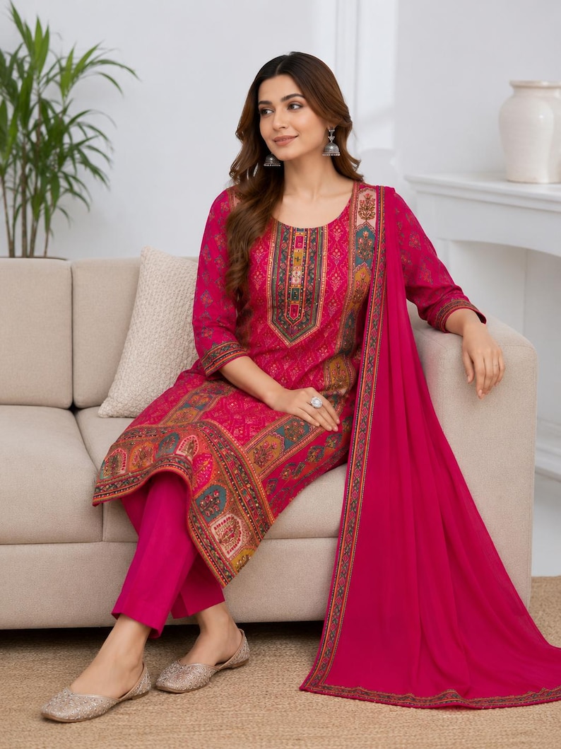 May include: A fuchsia three-piece outfit consisting of a long-sleeved tunic with a multi-colored geometric and floral print, solid fuchsia trousers, and a matching fuchsia dupatta with a decorative border along the edges.