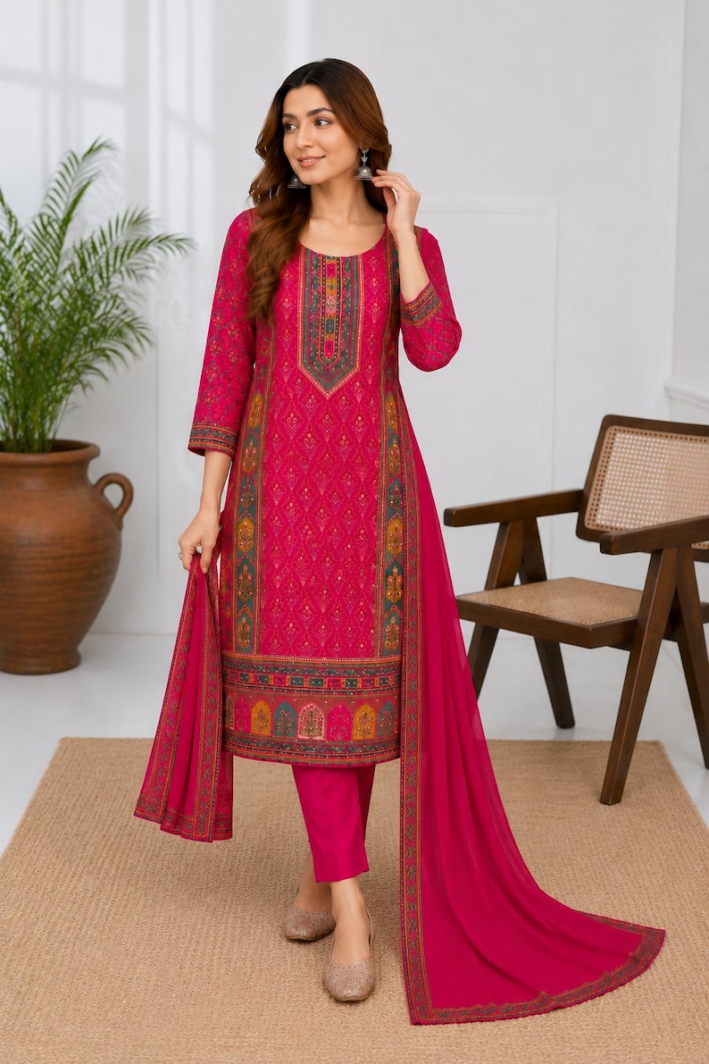 May include: A vibrant fuchsia three-piece ensemble featuring a knee-length tunic with intricate multi-colored geometric patterns along the neckline, cuffs, and hem, paired with matching solid fuchsia trousers and a long, lightweight fuchsia dupatta.