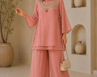 May include: A dusty rose tunic and wide-leg trousers set. The tunic features a collared neckline, flared sleeves, side drawstring ties, and a decorative embroidered yoke with metallic accents. The trousers are loose-fitting with a matching solid color.