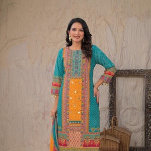 Puede incluir: Un salwar kameez bordado en color turquesa, naranja y rojo. La túnica de manga larga presenta intrincados patrones y adornos de espejo. El conjunto incluye un dupatta a juego y es adecuado para ocasiones festivas.