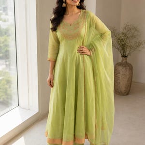 May include: A lime green A-line kurta set featuring three-quarter sleeves, a scoop neckline with intricate gold embroidery, and a matching sheer dupatta with a gold border. The ensemble includes wide-leg trousers in the same light green fabric.
