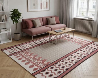May include: A rectangular area rug featuring a central light gray field with thin vertical stripes, bordered by wide bands of dusty rose and cream geometric patterns, including repeating diamond shapes and stylized floral motifs in dark brown.