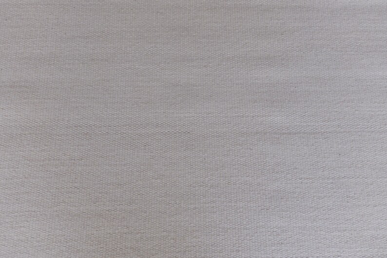 May include: A light gray fabric with a visible woven texture. The material features a consistent, tight grid pattern created by the interlacing of individual threads, resulting in a uniform, matte surface appearance across the entire frame.