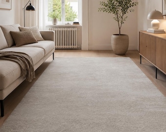 May include: A large, rectangular area rug in a solid light beige color with a soft, textured pile. The rug is positioned on a light-colored wooden floor, extending from the foreground toward the center of the room, covering a significant portion of the floor space.