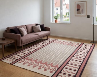 May include: A rectangular area rug featuring a central beige field with vertical stripes, bordered by wide bands in dusty rose and dark brown. The design includes repeating geometric patterns and stylized floral motifs along the edges.