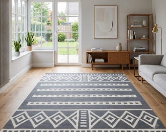 May include: A rectangular area rug featuring a dark gray background with a repeating white geometric pattern consisting of diamonds, horizontal stripes, and vertical bars. The rug is laid flat on a light-colored wooden floor in a bright room.