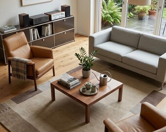 May include: A living room featuring a light gray sofa, two tan leather armchairs with wooden frames, and a square wooden coffee table. The table holds a small potted plant, a silver watering can, and a ceramic tea set on a round tray.