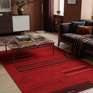 May include: A rectangular area rug featuring a vibrant red base with horizontal black and dark brown stripes. The rug includes thin, light-colored linear accents and a dark brown border at one end with a short, white fringe along the edge.