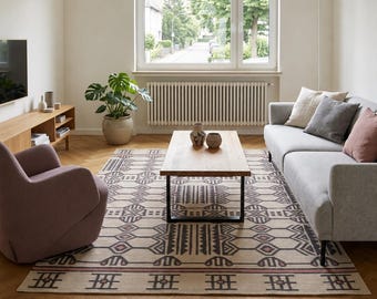 May include: A living room featuring a light gray sofa with beige, gray, and pink pillows, a mauve armchair, and a rectangular area rug with a geometric pattern in dark brown and pink on a cream background, centered under a wooden coffee table.