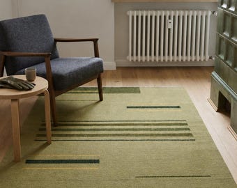 Puede incluir: Una alfombra rectangular con una base de color verde salvia y un patrón geométrico de rayas horizontales en tonos verde oliva oscuro, verde bosque y amarillo mostaza. La alfombra tiene una textura de pelo corto y flecos blancos en los extremos.