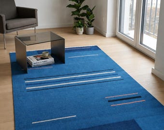 May include: A rectangular area rug featuring a vibrant blue base with horizontal stripes in white, dark blue, and soft orange. The rug has a flat-woven texture and is finished with short, cream-colored fringe along the two shorter edges.