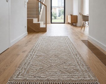 May include: A rectangular runner rug featuring a woven beige and white diamond pattern with intricate geometric borders and a fringed edge. The rug is positioned lengthwise on a light-colored wooden floor in a bright, open-plan interior space.