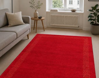 May include: A rectangular area rug in a vibrant solid red color featuring a decorative border with a repeating golden yellow geometric pattern. The rug has a soft, textured surface and is positioned flat on a light-colored wooden floor.