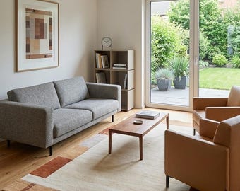 May include: A living room featuring a gray fabric sofa, two tan leather armchairs, and a rectangular wooden coffee table. A large area rug with geometric patterns in cream, brown, and orange sits on the floor. A wooden bookshelf and framed art.