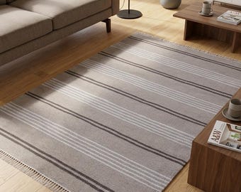 May include: A rectangular area rug featuring a light beige base with horizontal stripes in varying widths of dark brown and white. The rug has short, light-colored fringe detailing along the two shorter edges, creating a textured finish.