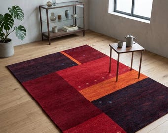 May include: A rectangular area rug featuring a geometric block pattern in shades of deep burgundy, bright red, and vibrant orange. The rug includes small, scattered embroidered motifs in contrasting colors across several of the colored sections.