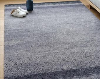 May include: A rectangular area rug featuring a gradient of gray and blue tones with a textured, mottled surface. The rug has darker horizontal bands near the edges with a subtle, repeating linear pattern integrated into the border design.