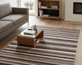 May include: A rectangular area rug featuring horizontal stripes in varying shades of brown, tan, cream, and dark gray. The rug has a soft, textured appearance with short white fringe detailing along the two shorter edges of the fabric.