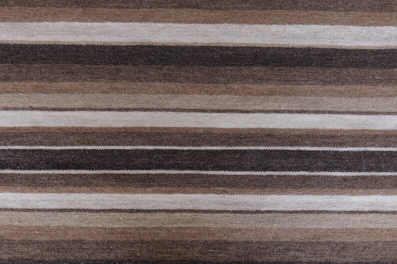 Puede incluir: Un tejido con un patr&oacute;n de rayas horizontales repetitivas en varios tonos de marr&oacute;n, beige, topo y blanco roto. La tela muestra un tejido texturizado y consistente con bandas oscuras y claras que se alternan por toda la superficie.