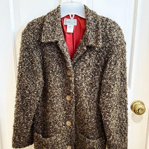 Peut inclure: Un manteau texturé marron et beige avec une doublure rouge. Le manteau a un col, deux poches avant et des boutons en bois. L'étiquette indique "SAKS FIFTH AVENUE FOLIO".