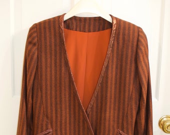 May include: Brown and black striped blazer with a double-breasted design. The blazer features gold buttons and a copper-colored lining. The lapel and pocket details have a metallic trim. The blazer is hanging on a white hanger.