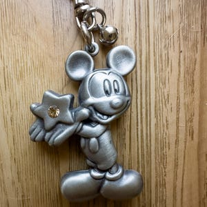 May include: Silver-toned Mickey Mouse keychain with a star charm featuring a clear rhinestone. The keychain has a silver-toned chain and a small bell.