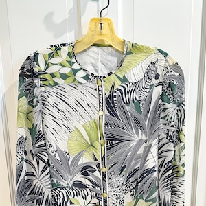 May include: A long-sleeved button-down shirt featuring a vibrant jungle-inspired print with zebras, leopards, and large tropical palm leaves in shades of forest green, lime green, black, and white. The garment has a round neckline and gold buttons.