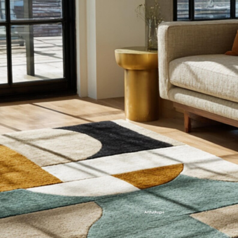 May include: A geometric patterned area rug with a black, mustard yellow, teal, and cream color scheme. The rug features a modern design with curved and angular shapes. The rug is placed on a hardwood floor, with a gold side table and a beige sofa in the background.