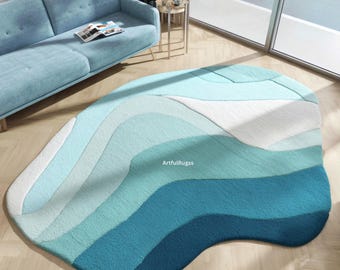 May include: A unique, abstract area rug with a layered design in shades of blue and white. The rug has a soft, textured appearance and a free-form shape, adding a modern touch to the room. The rug is placed on a hardwood floor.