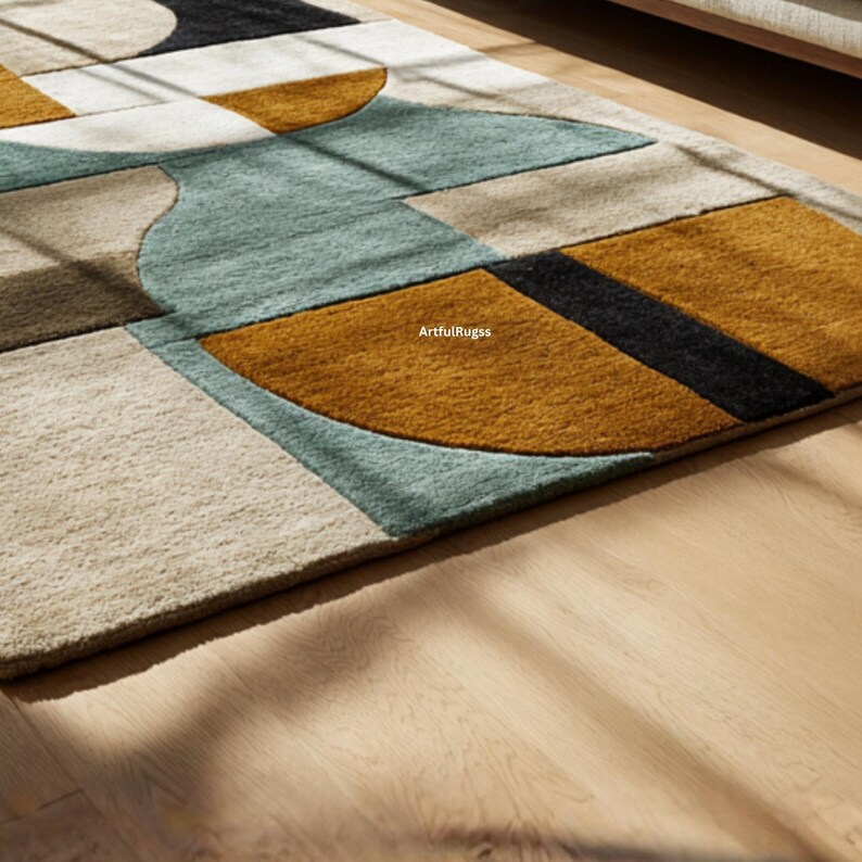 May include: Geometric patterned area rug featuring a mix of shapes and colors. The rug has a beige, teal, brown, black, and gold color scheme. The rug is made of a soft, textured material and is placed on a wooden floor.