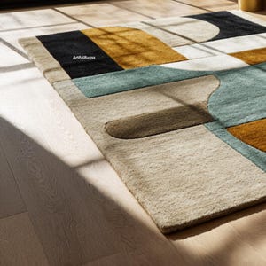 May include: A geometric area rug with a modern design. The rug features a beige background with sections of black, gold, teal, and brown. The rug is rectangular and has a soft, textured appearance. The rug is placed on a light-colored wooden floor.