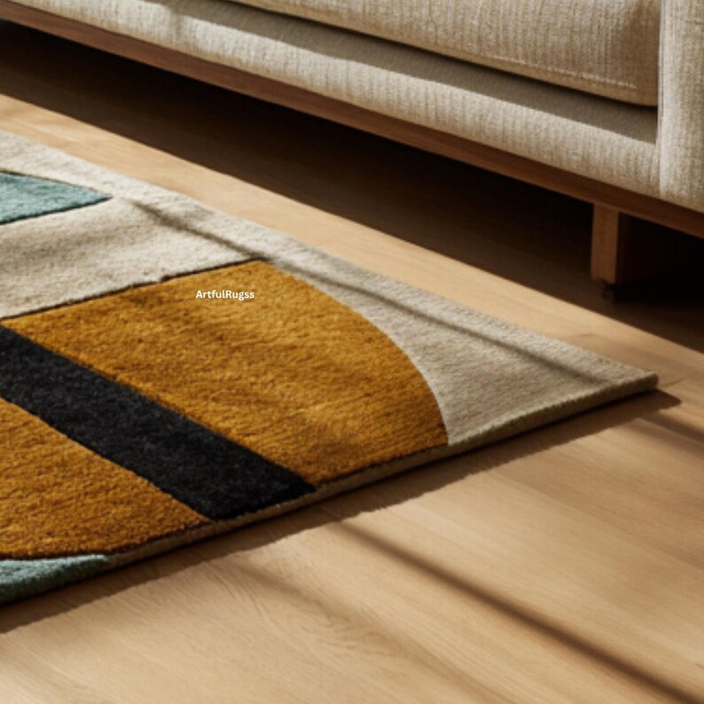 May include: Geometric patterned rug with a color block design. The rug features a mustard yellow, black, teal, and beige color scheme. The rug is placed on a hardwood floor, with a portion of a beige sofa visible in the background.