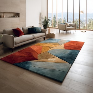 May include: A large, rectangular area rug with a geometric design in shades of red, orange, yellow, blue, and gray. The rug is placed on a hardwood floor in a living room setting, with a sofa and armchair visible.