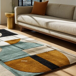 May include: Geometric patterned area rug with a modern design. The rug features a combination of colors including teal, mustard yellow, black, and beige. The rug is placed on a hardwood floor, with a sofa and side table in the background.