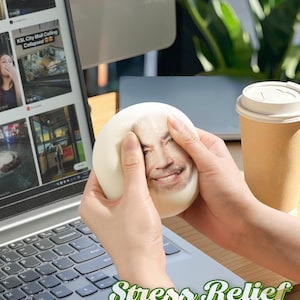 May include: A white stress ball with a printed face is squeezed between two hands. The text "Stress Relief" and "Personalized funy!" is displayed on the laptop. A laptop, coffee cup, and plant are in the background.