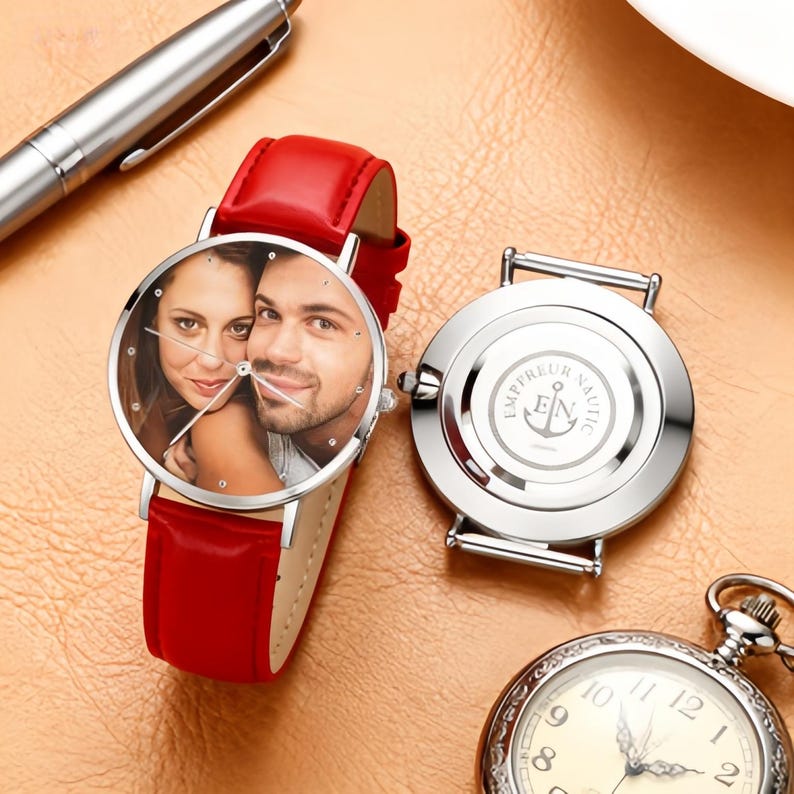 May include: A red leather strap watch with a silver case and a custom photo on the face. The watch face features a photo of a couple. The watch is next to a silver pen and a pocket watch.