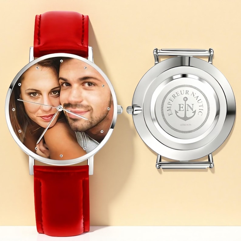 May include: A silver wristwatch with a red leather band. The watch face features a photo of a couple. The back of the watch is silver with the words "EMPEREUR NAUTIC" and an anchor logo.
