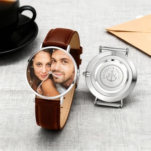 May include: A personalized wristwatch with a brown leather band. The watch face displays a color photograph of a couple. The watch's back is silver with the words "EMPEREUR NAUTIC" and an anchor symbol.