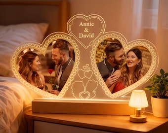 Könnte beinhalten: Ein personalisierter herzförmiger Fotorahmen mit den Namen "Annie & David". Er ist mit warmem Licht beleuchtet und zeigt zwei Fotos eines Paares. Er steht auf einem Holzsockel, mit einer kleinen Lampe und einer Topfpflanze daneben.