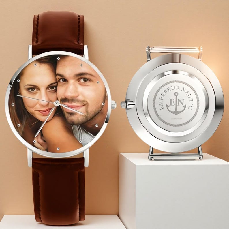 May include: A silver wristwatch with a brown leather band. The watch face displays a color photograph of a couple. The back of the watch is visible, with the words "EMPEREUR NAUTIC" and an anchor logo.