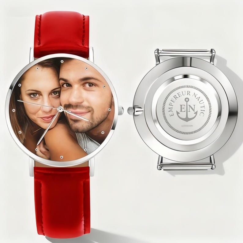 May include: A silver wristwatch with a red leather band. The watch face displays a color photo of a couple. The back of the watch is silver with the words "EMPEREUR NAUTIC" and an anchor logo.