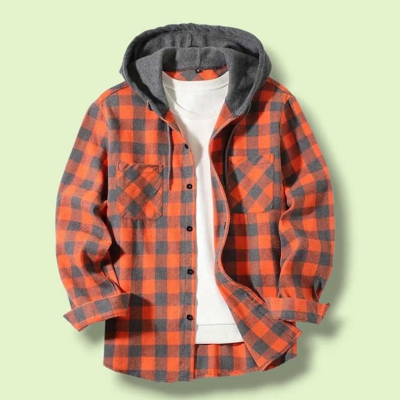 May include: A long-sleeved button-down shirt featuring an orange and charcoal gray plaid pattern. The garment includes a solid charcoal gray hood with drawstrings and a white undershirt layer visible at the neckline and front opening.