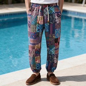 Könnte beinhalten: Jogginghose mit einem lebendigen Patchwork-Design aus verschiedenen Paisley-, Blumen- und geometrischen Mustern in Blau-, Lila-, Rot- und Grüntönen. Die Hose verfügt über einen elastischen Bund mit dicken weißen Kordelzügen und braunen Perlen.