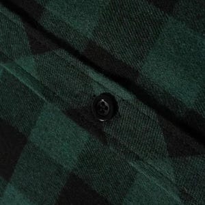 May include: A dark green and black buffalo plaid flannel shirt featuring a textured fabric weave and a single centered black four-hole button on a vertical placket. The material displays a soft, brushed finish with a classic checkered pattern.
