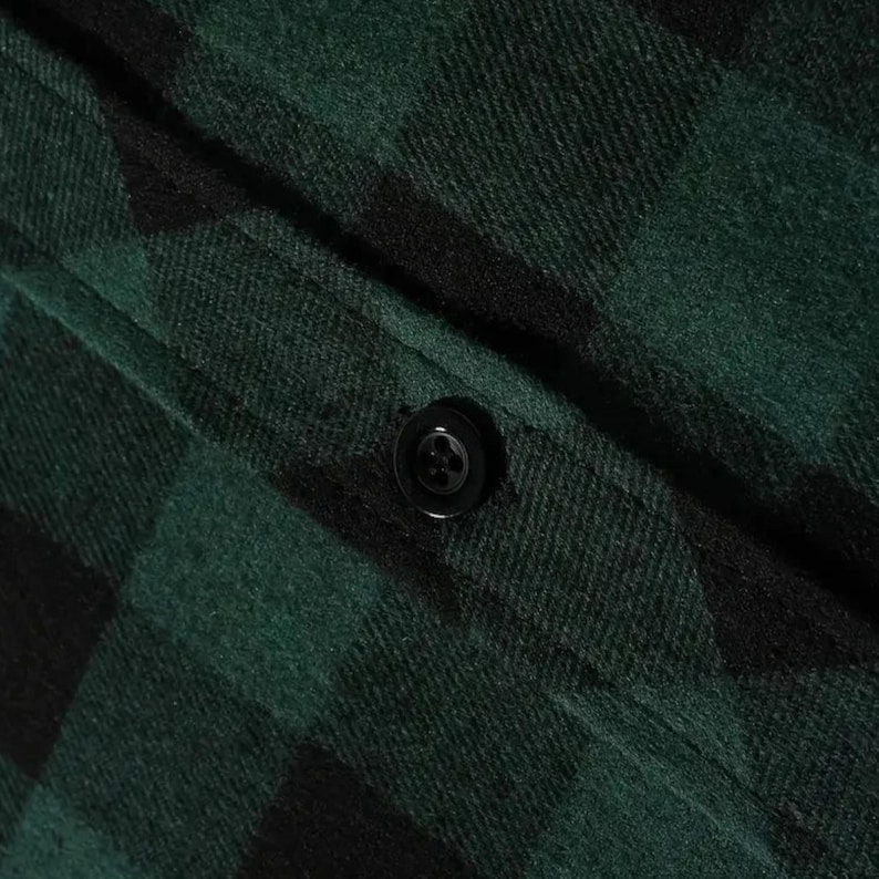 May include: A dark green and black buffalo plaid flannel shirt featuring a textured fabric weave and a single centered black four-hole button on a vertical placket. The material displays a soft, brushed finish with a classic checkered pattern.